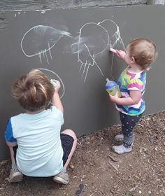 Two children drawing with chalk on an outdoor chalkboard.