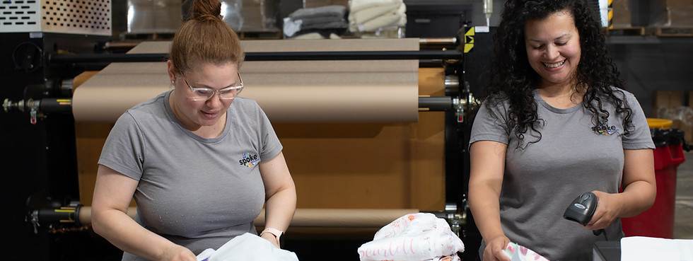 Two women packaging printed goods to prepare them for shipping at the Spoke facility