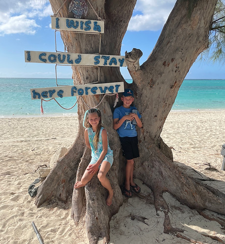 Two kids under an "I wish I could stay here forever" sign on the beach at Beaches Turks and Caicos family all-inclusive resort