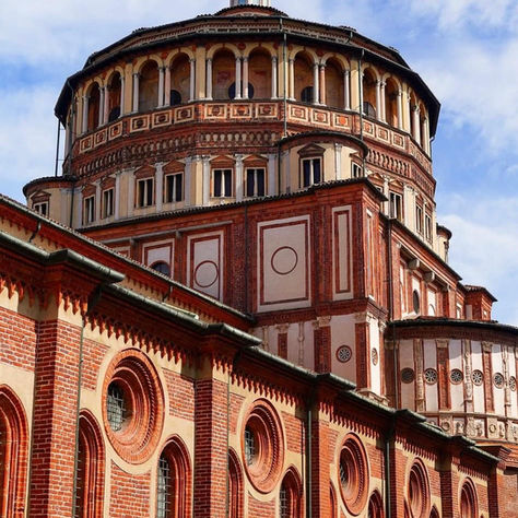 Église gothique en briques rouges avec grande coupole et clocher, vue de bas sous ciel bleu nuageux à Milan.