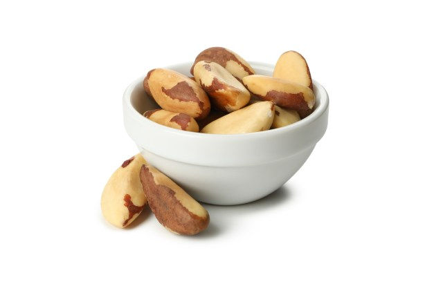 fundo branco com pote de porcelana com castanhas do pará dentro de fora do pote