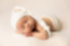 A baby sleeps on a cream colored backdrop during a studio newborn portrait session_