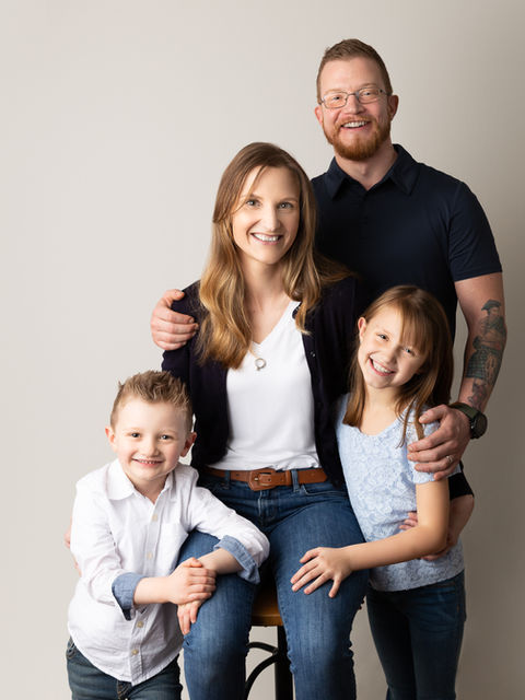 A family of 4 smiles during a studio photo shoot with Ashley Stack Photography.