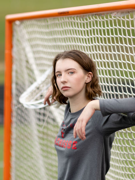 A girl poses with a lacrosse stick and net during a senior photo shoot