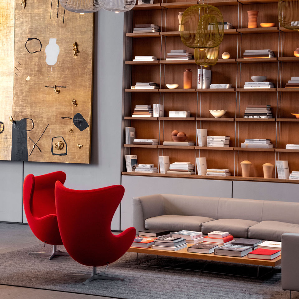 High ceilings with a gorgeous book shelf that is lined with designers books. Contemporary red chairs surround a large coffee table adorned with books.