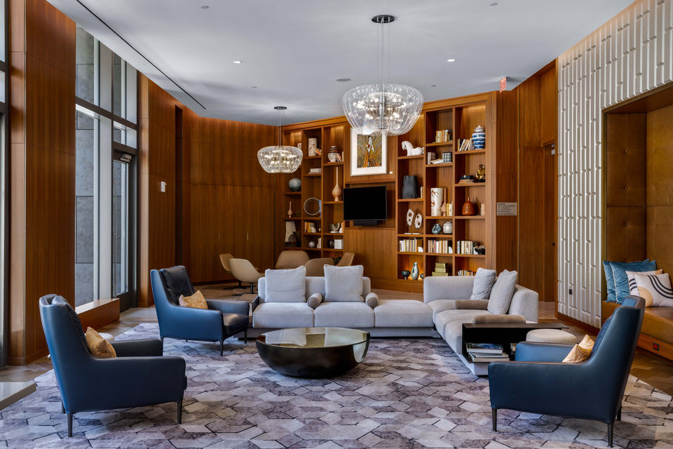 Floor to ceiling windows light a large lounge that is filled with leather chairs and light grey sectional sofa. Built in book shelfs host decorations and stylish books.