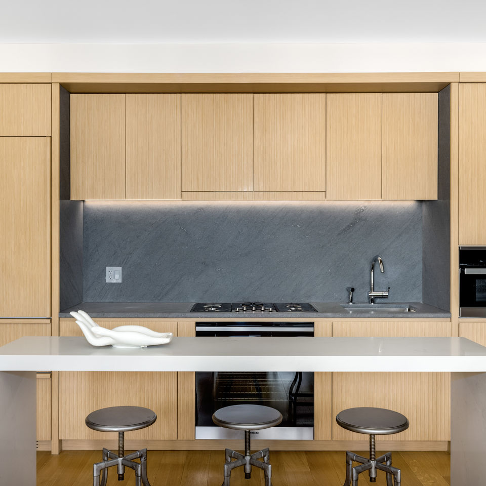 A modern kitchen with light brown wood paneling and white marble breakfast bar.