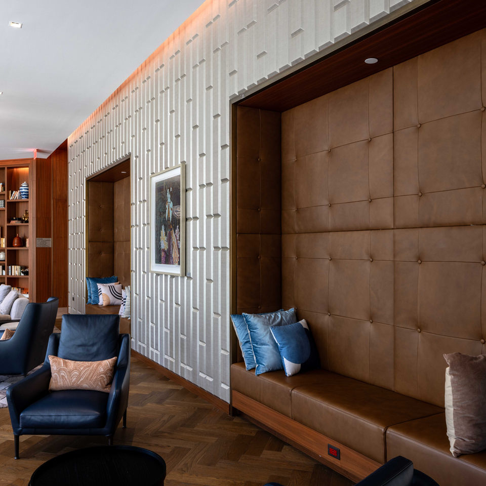 Floor to ceiling windows light a large lounge that is filled with leather chairs and light grey sectional sofa. Built in book shelfs host decorations and stylish books.