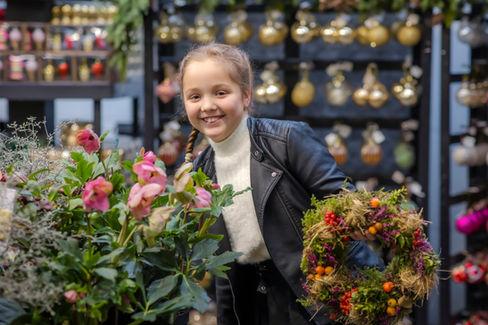 Pikkutyttö kurkkaa Viherlassilan ihanien joulukukkien takaa.