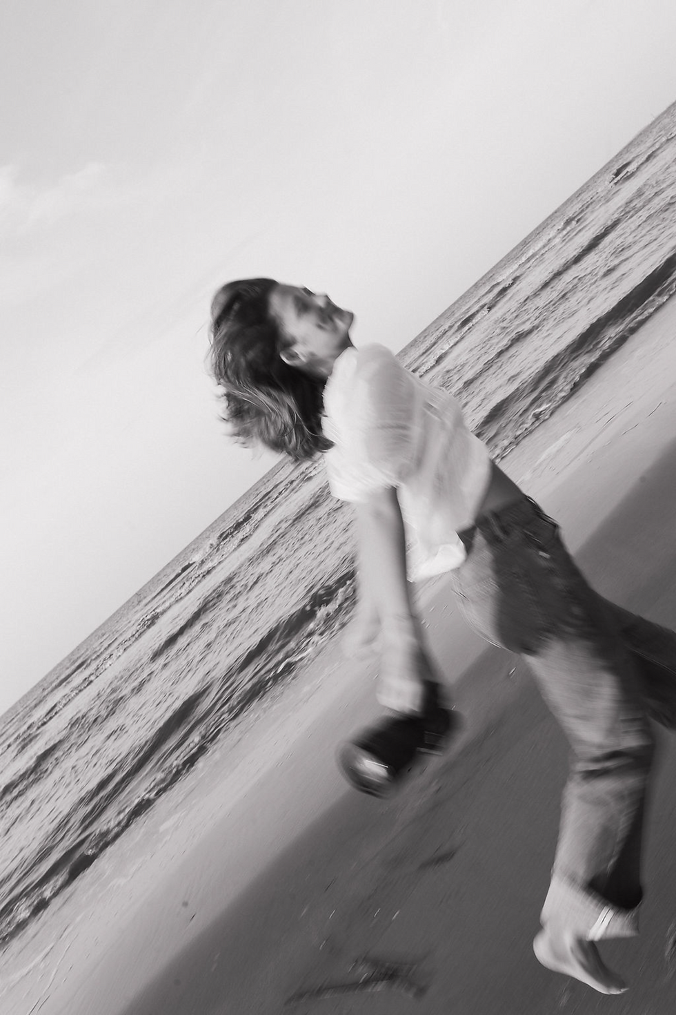 Black and white photo of Grace standing on the beach, wind blowing through her hair