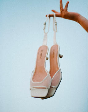 Cream slingback heels held up against a pale blue sky.