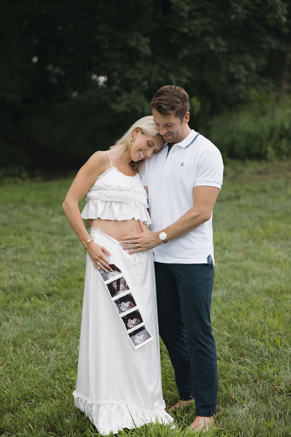Couple embracing outdoors, holding sonogram photos, maternity announcement