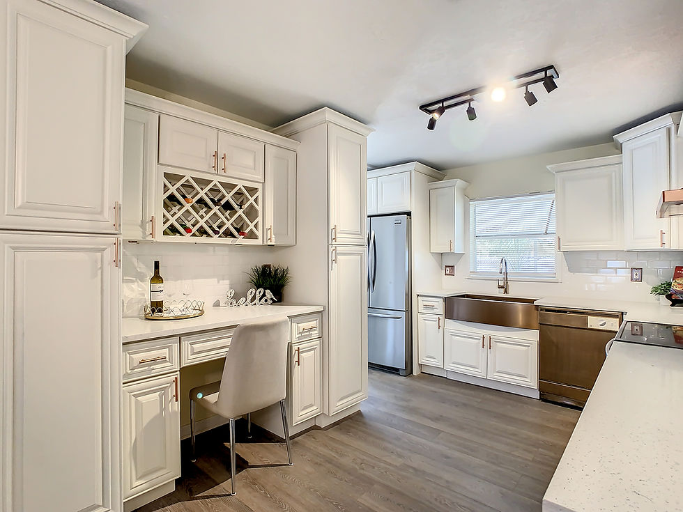 Bright modern pearl white kitchen with wine rack, desk nook, stainless fridge and dishwasher, lit by track lights.