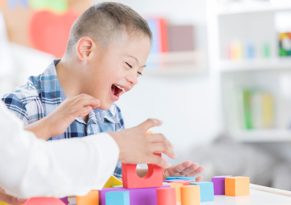 Joyful boy with Down syndrome laughing, playing colorful blocks with adult.