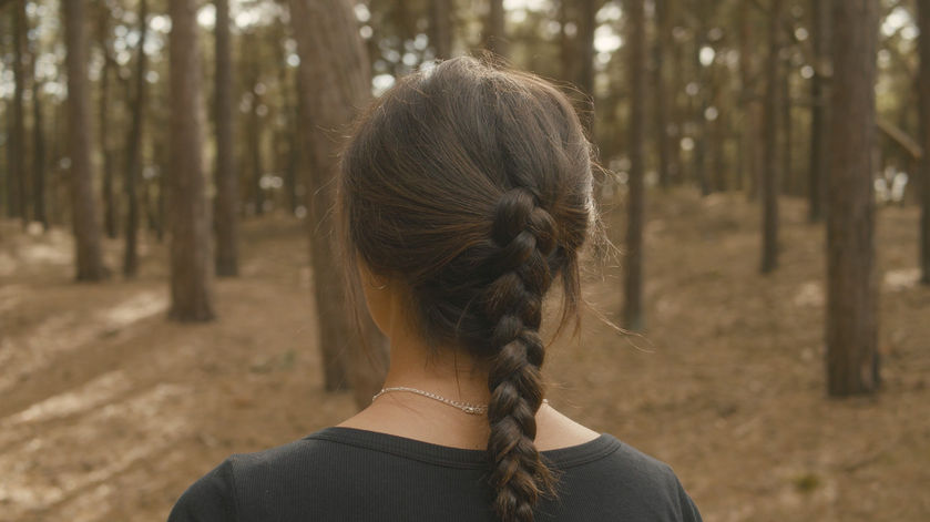 A young woman stands outdoors in a woodland landscape