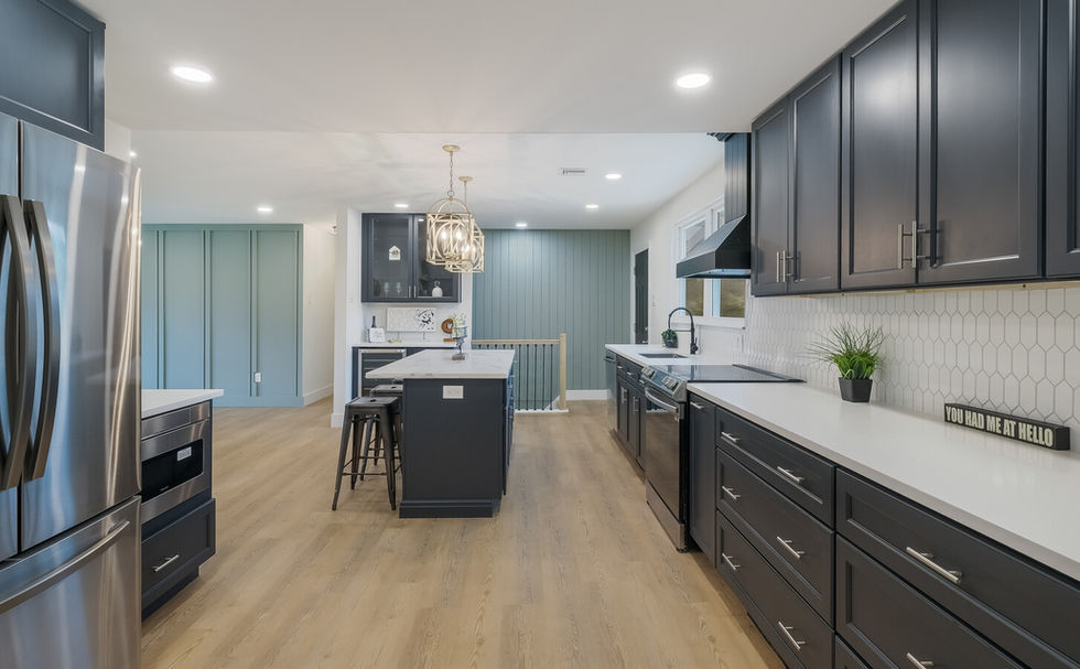 A view of a modernized kitchen with black cabinets, white backsplash and a sage green accent wall