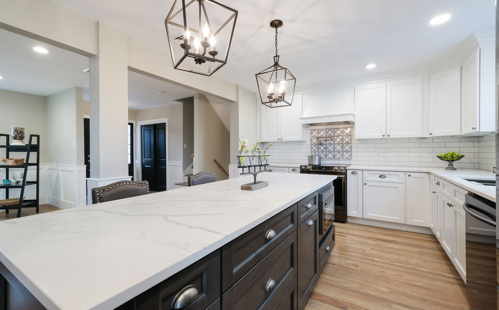 Large kitchen island with marbled white countertops and black cabinetry underneath two bright hanging ceiling lights