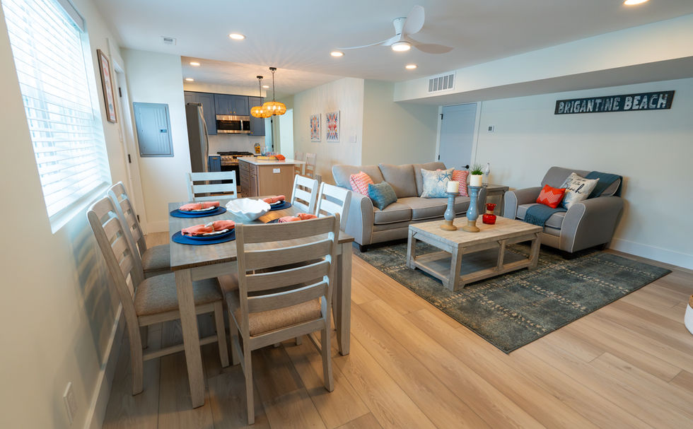 Coastal designed, open interior of furnished living room, dining set, and kitchen