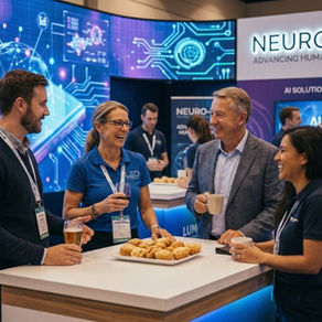 People at a tech expo booth with "NEURO-LINK" displayed. They chat and laugh over food and drinks, surrounded by digital screens and exhibits.