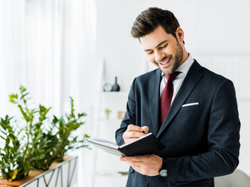 bel homme d'affaires souriant en tenue formelle écrivant dans un cahier au bureau