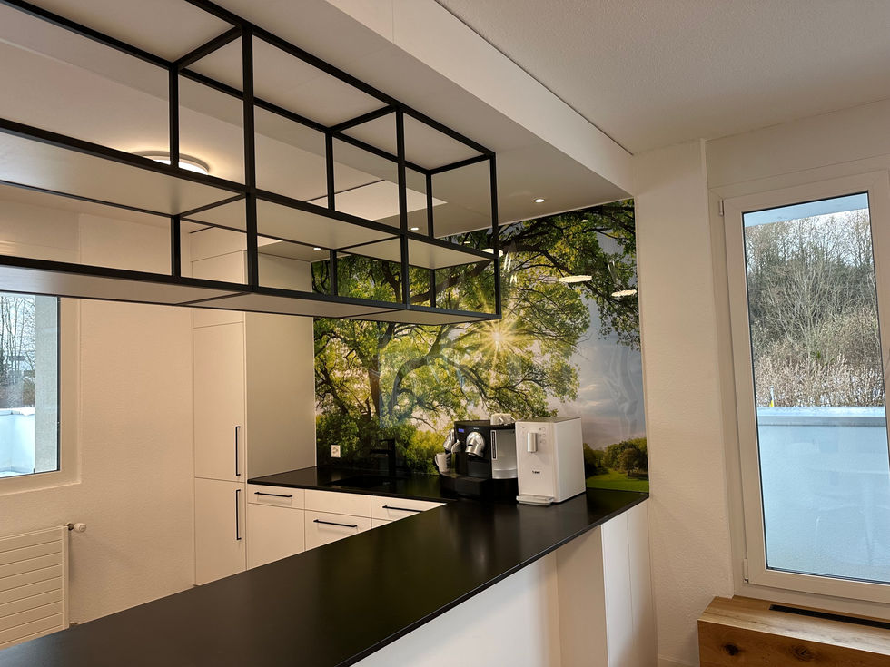 Das Bild zeigt eine weiße Küche mit schwarzen Griffen und einem heruntergehängten Deckenregal. Die Küche wirkt modern und elegant.
