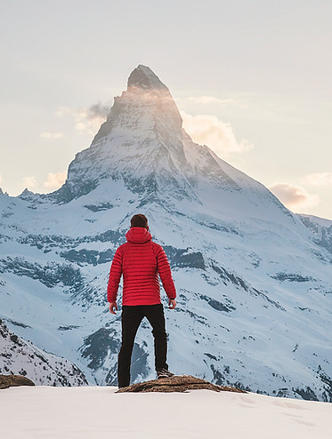 Personne en manteau rouge faisant face à la montagne, représentant les défis à affronter