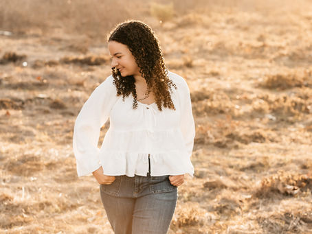 high school senior young lady getting her photos taken in golden sunlight in a field