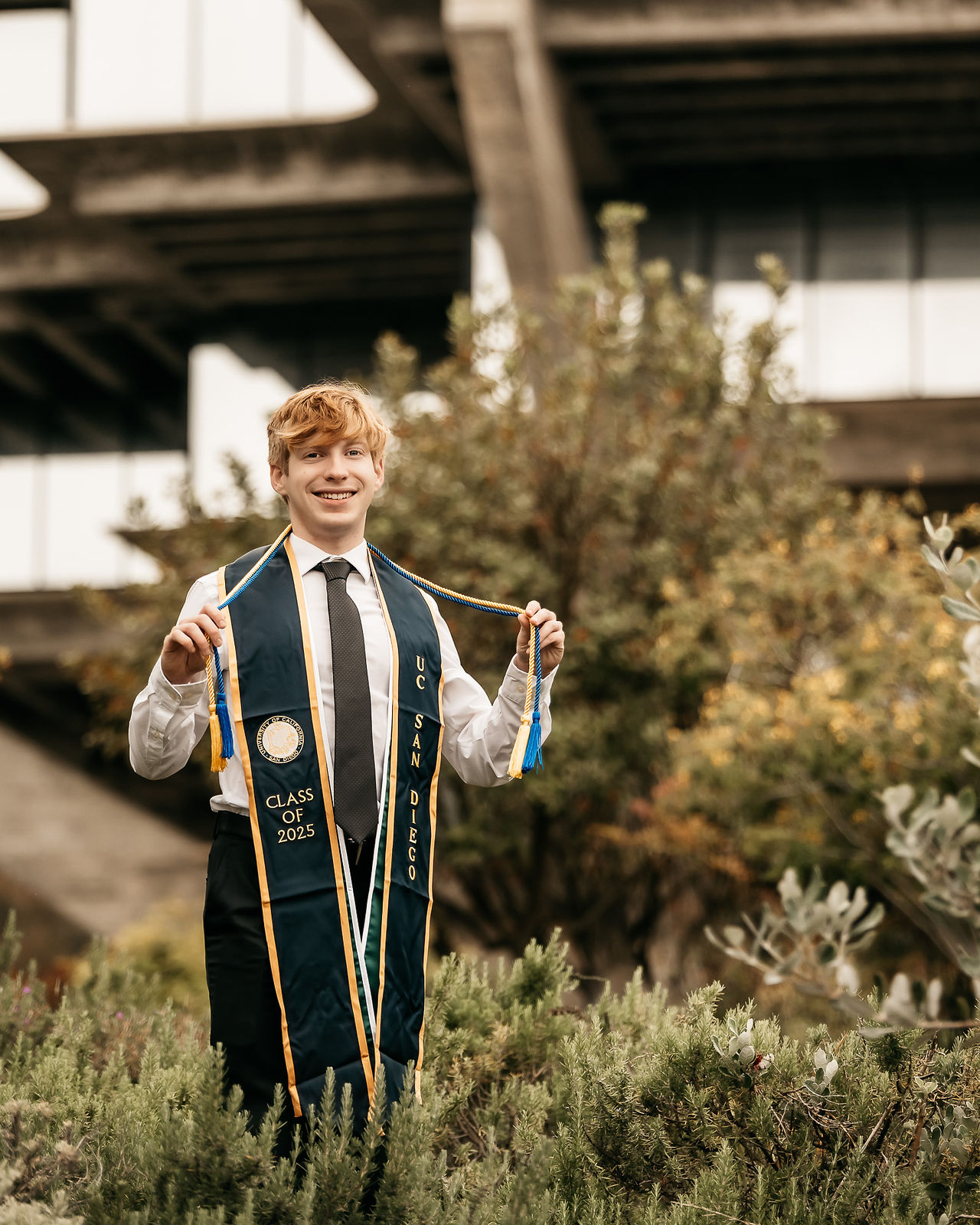 UCSD senior graduate in cap and gown smiling during solo graduation photo session on campus at University of California San Diego.