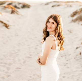 Senior portrait of high school girl in white dress on coastal dunes during golden light, San Diego senior photographer.