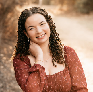 Close-up senior portrait of smiling high school senior with curly hair in a burgundy dress, warm golden hour light, San Diego senior photographer.