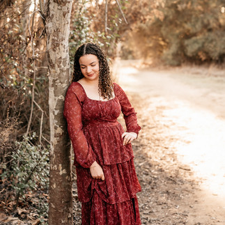 High school senior walking through a sunlit field in a flowing burgundy dress at sunset, golden light outdoor senior photos in San Diego.