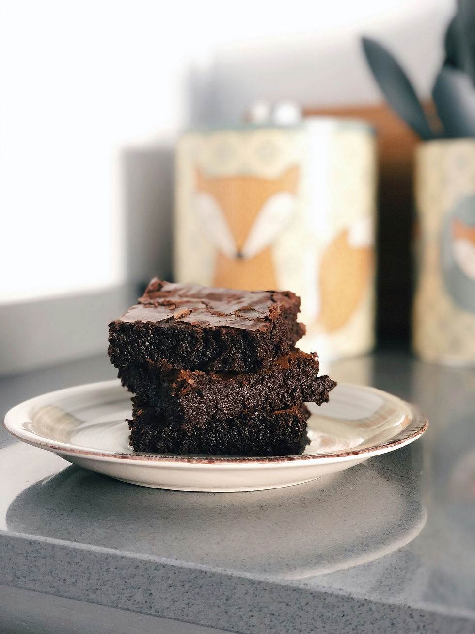 a plate of chocolate brownies on a counter with a fox patterened biscuit tin in the background