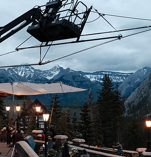 Outdoor film production set with camera crane overlooking scenic mountain landscape and pine forest at dusk."