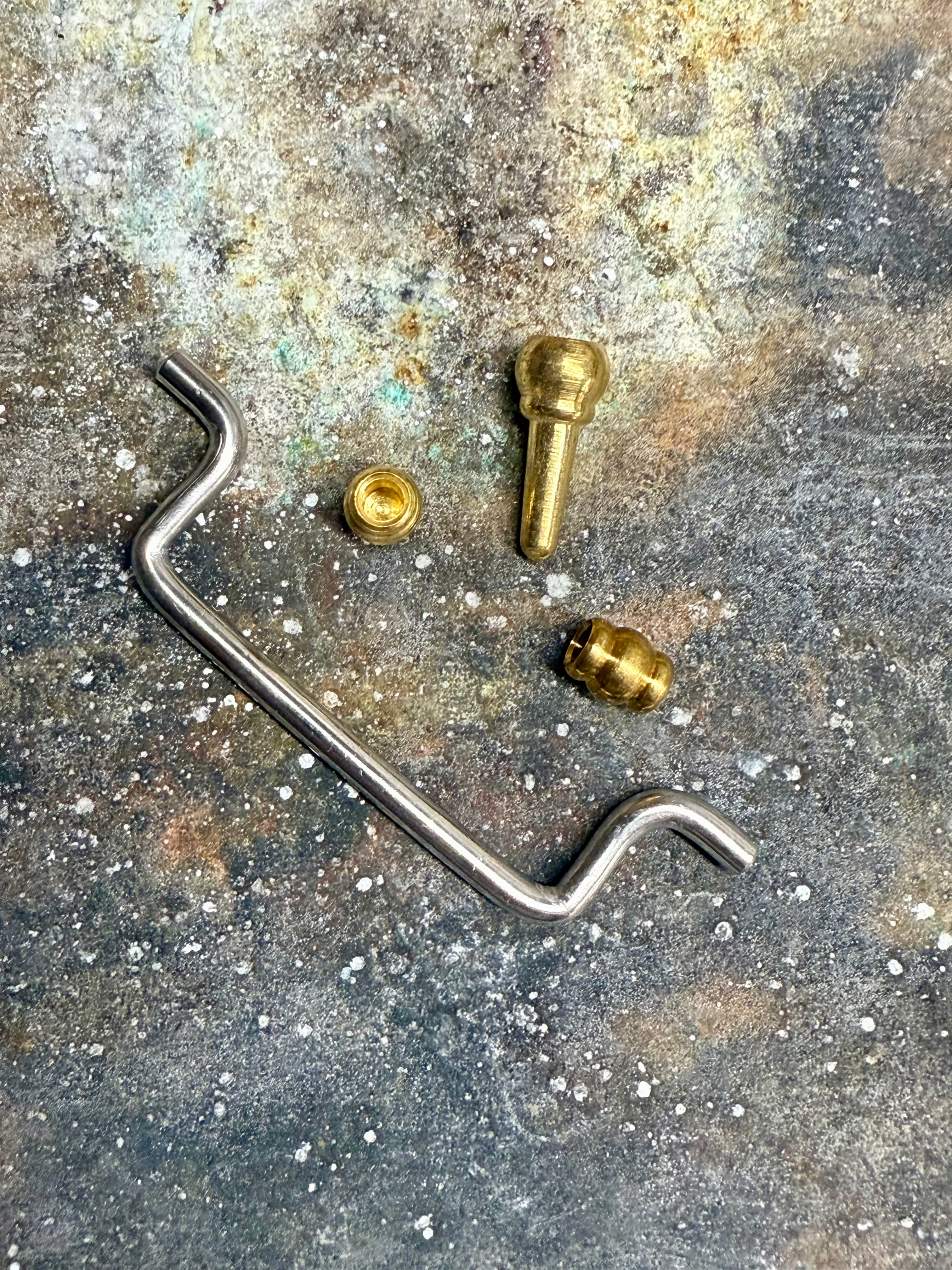 Various jewelry making tools on a textured surface, including a hook and brass pieces.