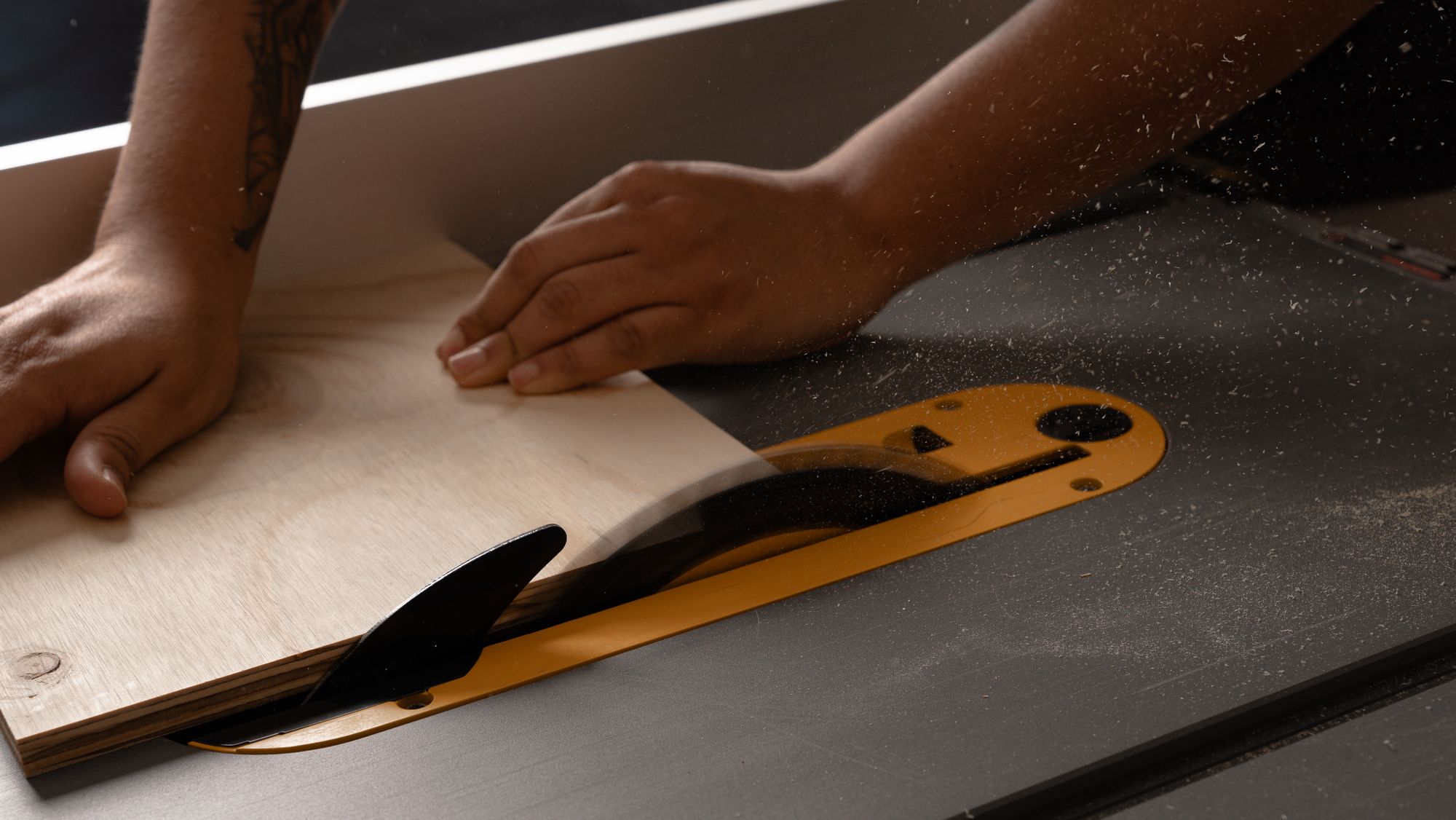 Hands guiding a wood panel through a table saw