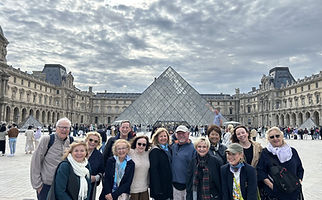 A group tour posing in front of the Louvre in Paris