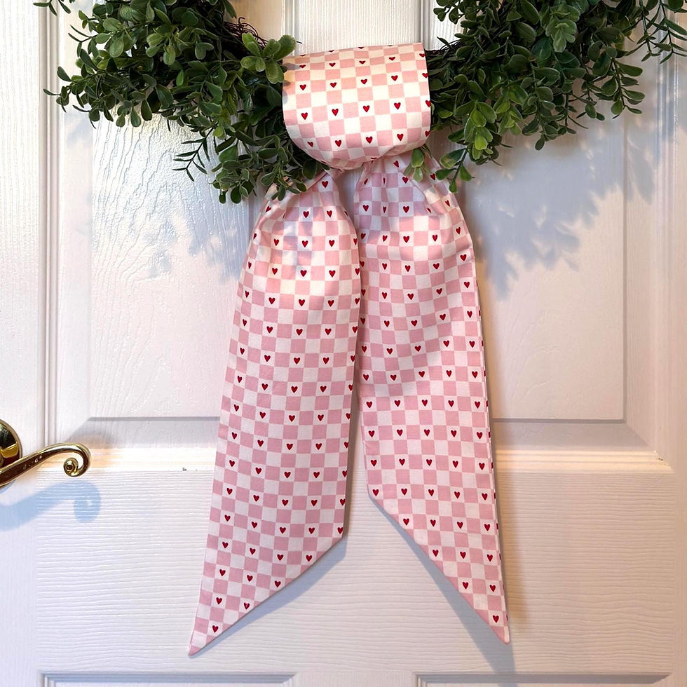 Thumbnail: Pink and white Valentine wreath sash with heart check pattern draped over a boxwood wreath on a white door.