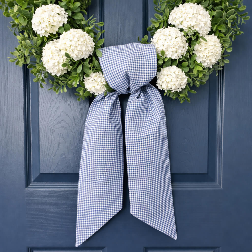 Blue and White small checked gingham simple knot wreath sash tied on a green boxwood wreath on a blue door.