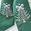 Thumbnail: Classic green embroidered Christmas wreath sash tied in a simple knot on a fresh evergreen wreath, displayed on a white panel