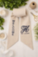 Personalized linen wreath sash with monogram tied on a boxwood wreath on a navy front door.