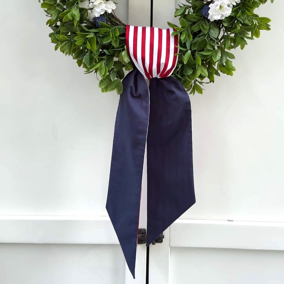 Thumbnail: red white and blue patriotic reversible wreath sash tied in a simple knot on a green boxwood wreath on a white door