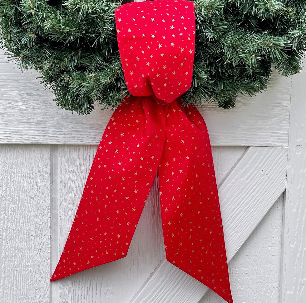 Close-up of a red Christmas wreath sash with metallic gold stars, styled on a green evergreen wreath. Handmade fabric sash ad