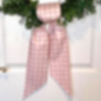 Pink and white Valentine wreath sash with heart check pattern draped over a boxwood wreath on a white door.