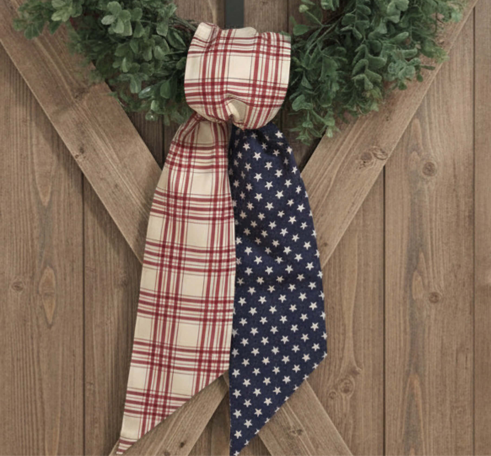 Americana reversible wreath sash styled on a door with a green wreath, featuring cream and red plaid fabric and blue stars