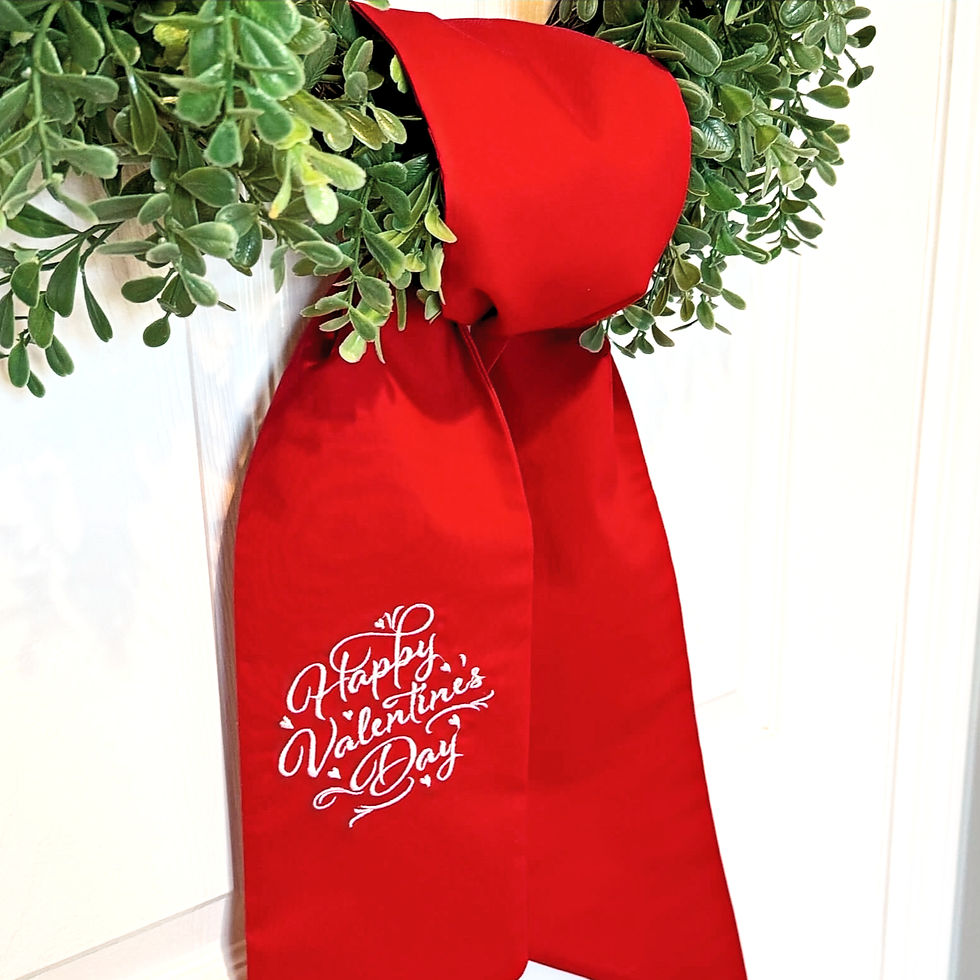 Green boxwood wreath with a bright red Valentine’s Day wreath sash tied in a bow on a white front door, white script embroide