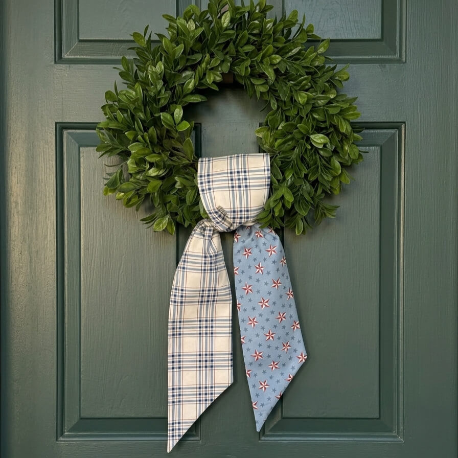 Reversible blue plaid patriotic wreath sash featuring Americana star fabric draped over a green front door wreath for summer