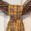 Thumbnail: Close-up of a gold and gray plaid Simple Knot wreath sash tied on a grapevine wreath, showing fabric texture and rustic fall