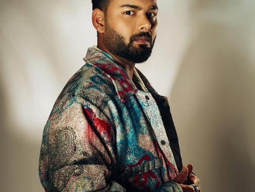 Man in colorful patterned jacket poses against blurred neutral background, with thoughtful expression, highlighting texture and detail.