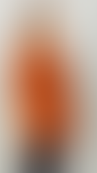 Smiling woman in red polka dot dress with fringe details, standing against a plain gray background. She exudes a cheerful mood.