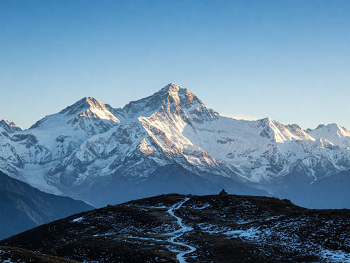 Snow-capped mountain peaks under a clear blue sky, with a winding path on a dark hill in the foreground. Peaceful and majestic scene.